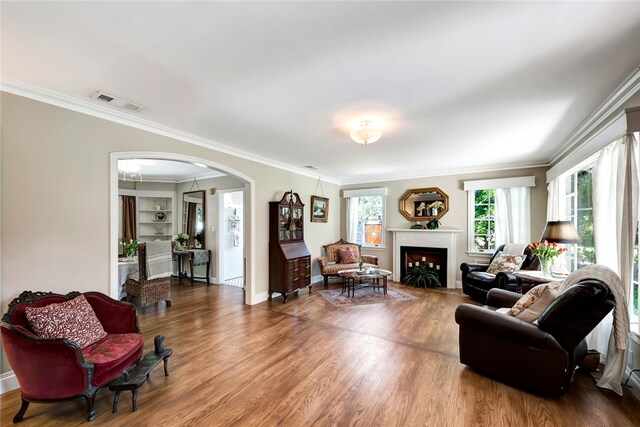 living room featuring built in shelves, wood-type flooring, and crown molding