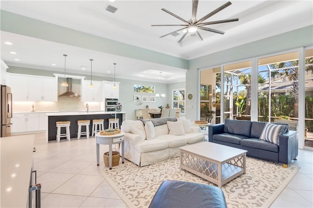 tiled living room with ceiling fan, crown molding, sink, and a tray ceiling