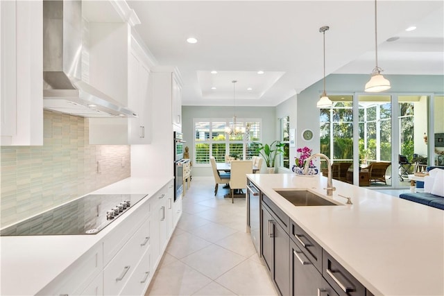 kitchen with white cabinets, wall chimney range hood, sink, appliances with stainless steel finishes, and a tray ceiling