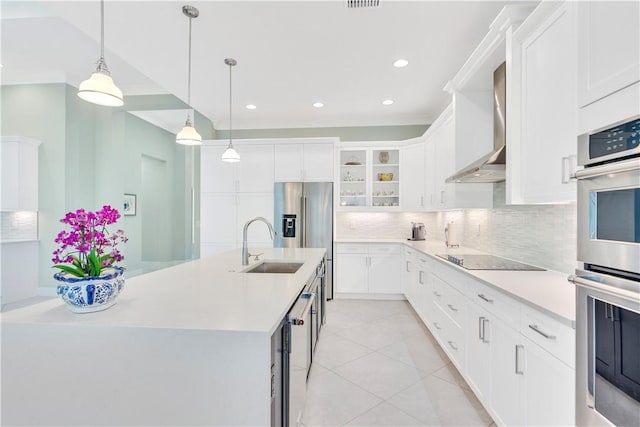 kitchen featuring wall chimney range hood, pendant lighting, a kitchen island with sink, white cabinets, and appliances with stainless steel finishes