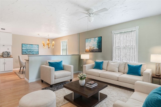 living room with ceiling fan with notable chandelier, light hardwood / wood-style flooring, and a wealth of natural light