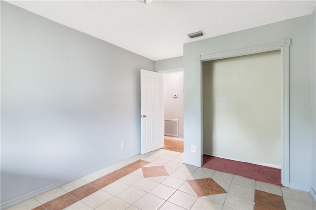 unfurnished bedroom featuring light tile patterned flooring, a textured ceiling, and a closet