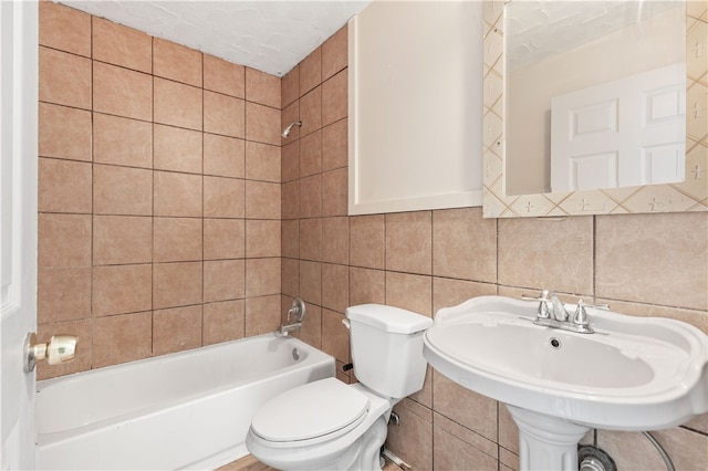 bathroom featuring a textured ceiling, toilet, tile walls, and tiled shower / bath