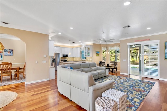 living room featuring ceiling fan, ornamental molding, and light wood-type flooring