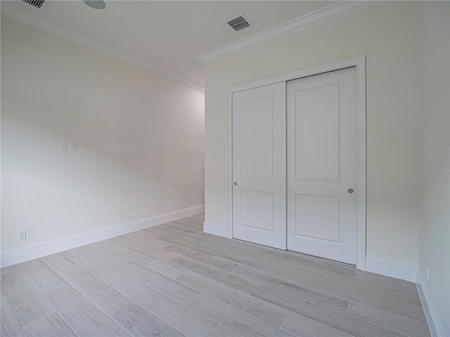 unfurnished bedroom featuring light hardwood / wood-style flooring, ornamental molding, and a closet