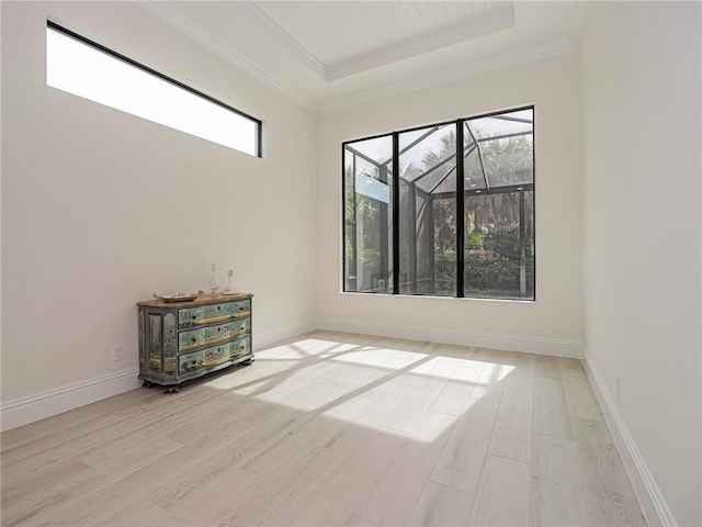 spare room with crown molding, a raised ceiling, and light hardwood / wood-style floors