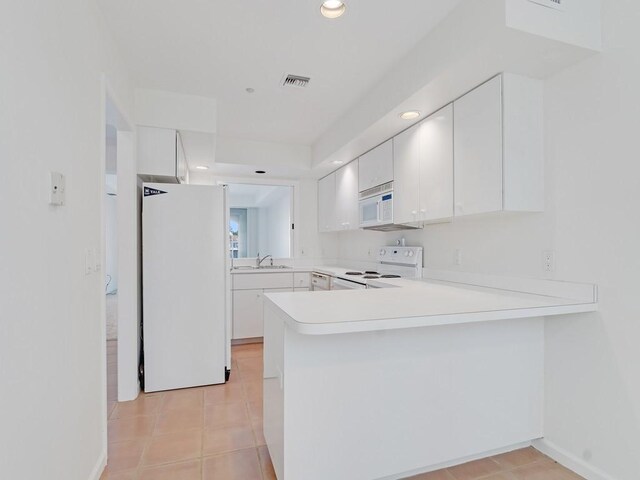 5540 N Harbor Village Dr Unit 103, Vero Beach, FL 32967 - kitchen featuring white appliances, a peninsula, light countertops, light tile patterned floors, and white cabinets