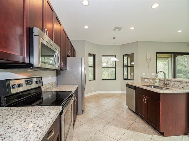 kitchen featuring appliances with stainless steel finishes, light stone counters, sink, light tile patterned floors, and hanging light fixtures