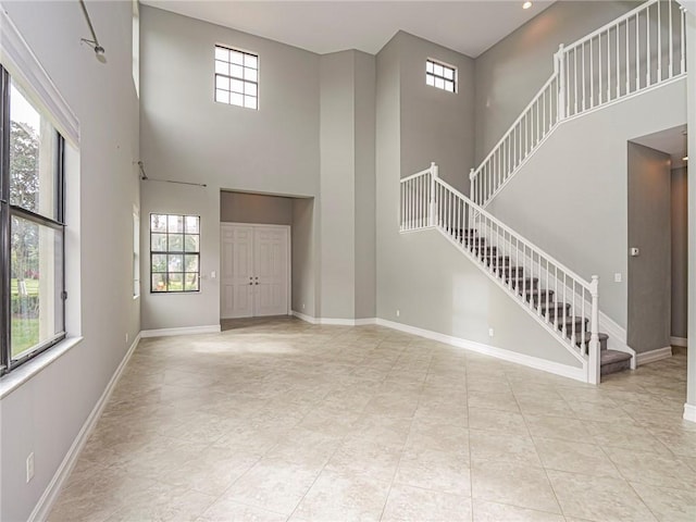 unfurnished living room with a wealth of natural light, a towering ceiling, and light tile patterned floors