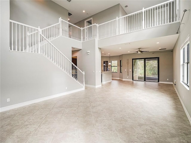 unfurnished living room with ceiling fan, tile patterned flooring, and a towering ceiling