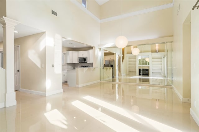 unfurnished living room featuring light tile patterned floors, a high ceiling, and decorative columns