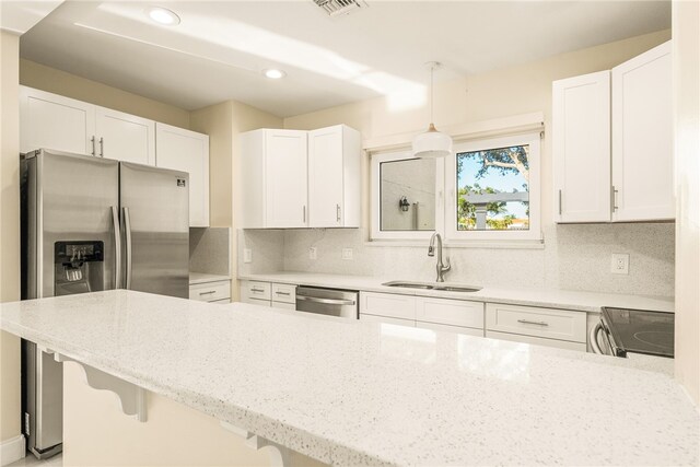 kitchen with sink, appliances with stainless steel finishes, light stone countertops, decorative light fixtures, and white cabinets