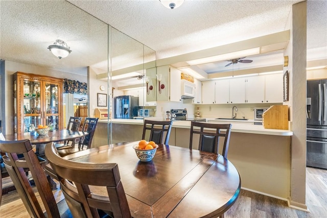 dining area with light wood finished floors, ceiling fan, a toaster, and a textured ceiling