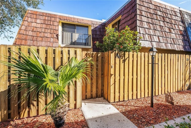 view of side of property featuring fence and mansard roof