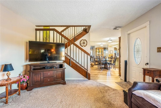 living area featuring light carpet, stairs, visible vents, and a textured ceiling