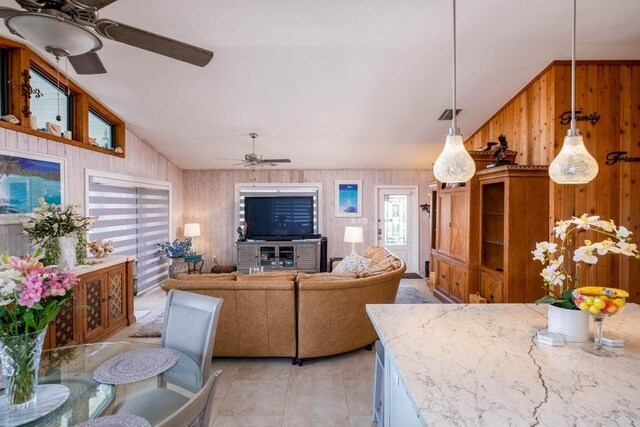 living room featuring ceiling fan, wooden walls, and vaulted ceiling
