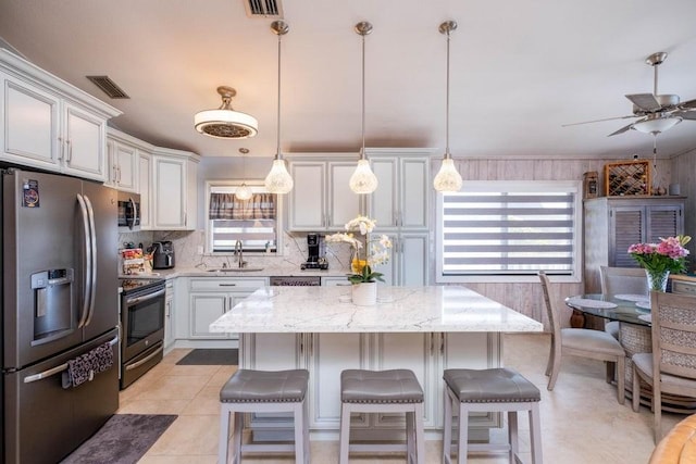 kitchen featuring stainless steel appliances, backsplash, ceiling fan, a center island, and a sink