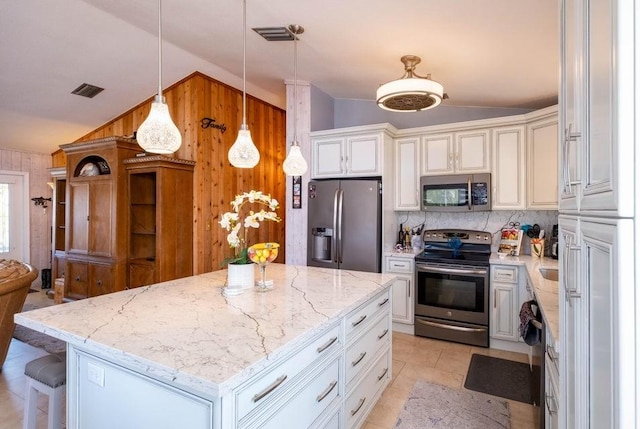 kitchen featuring appliances with stainless steel finishes, vaulted ceiling, wood walls, light stone countertops, and a center island