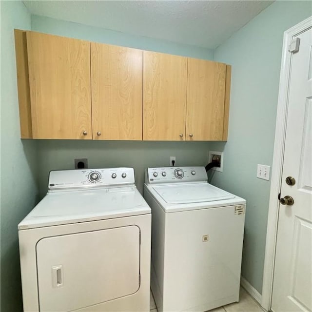 laundry area featuring washing machine and dryer, light tile patterned flooring, cabinet space, and baseboards