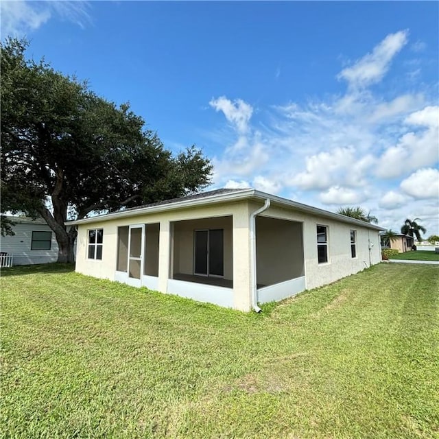 rear view of house featuring a yard and stucco siding