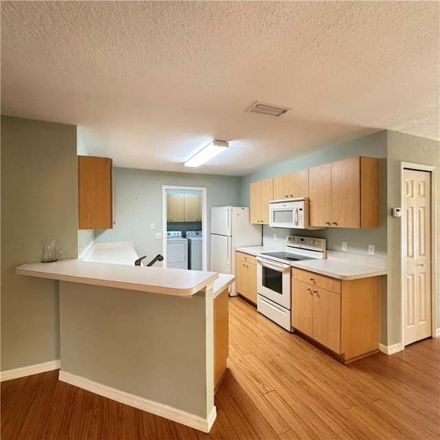 kitchen with washer and dryer, white appliances, light wood-style floors, a peninsula, and light countertops