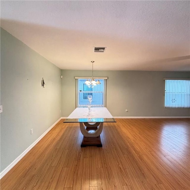 unfurnished dining area with baseboards, a notable chandelier, wood finished floors, and a textured ceiling