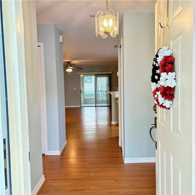 corridor with light wood-type flooring, baseboards, and a chandelier