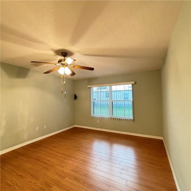 empty room featuring a textured ceiling, wood finished floors, baseboards, and ceiling fan