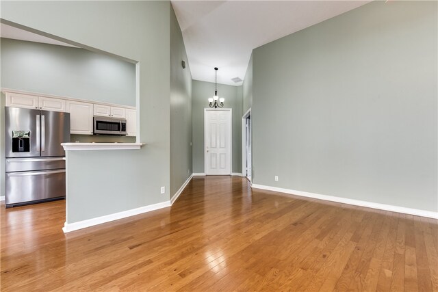 interior space featuring appliances with stainless steel finishes, an inviting chandelier, high vaulted ceiling, white cabinets, and light hardwood / wood-style floors