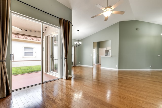 empty room with ceiling fan with notable chandelier, light wood-type flooring, and vaulted ceiling