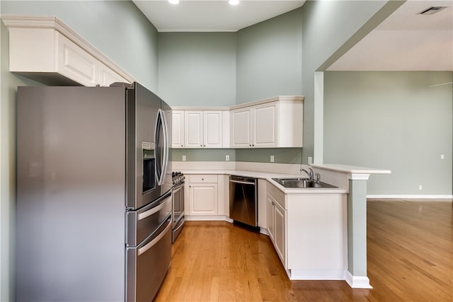 kitchen with sink, stainless steel appliances, kitchen peninsula, light hardwood / wood-style floors, and white cabinets