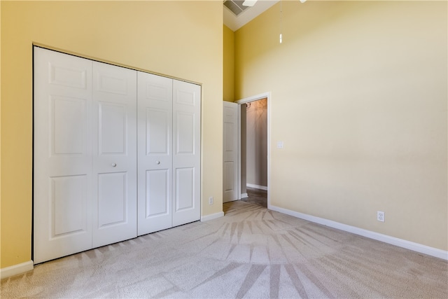 unfurnished bedroom featuring light carpet, a high ceiling, and a closet