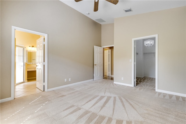 unfurnished bedroom with light carpet, ceiling fan, a spacious closet, connected bathroom, and a closet