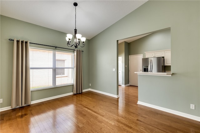 unfurnished room featuring light hardwood / wood-style floors, vaulted ceiling, and a notable chandelier