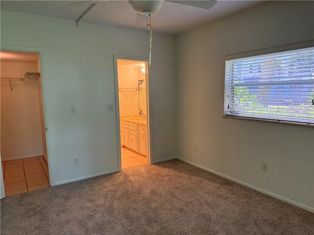 unfurnished bedroom with ceiling fan, light colored carpet, ensuite bath, a spacious closet, and a closet