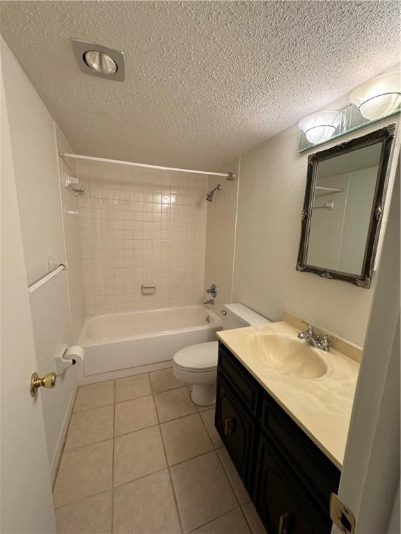 full bathroom with a textured ceiling, tiled shower / bath, tile patterned floors, vanity, and toilet