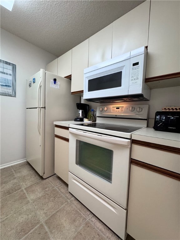 kitchen with white appliances, white cabinetry, light tile patterned floors, and a textured ceiling