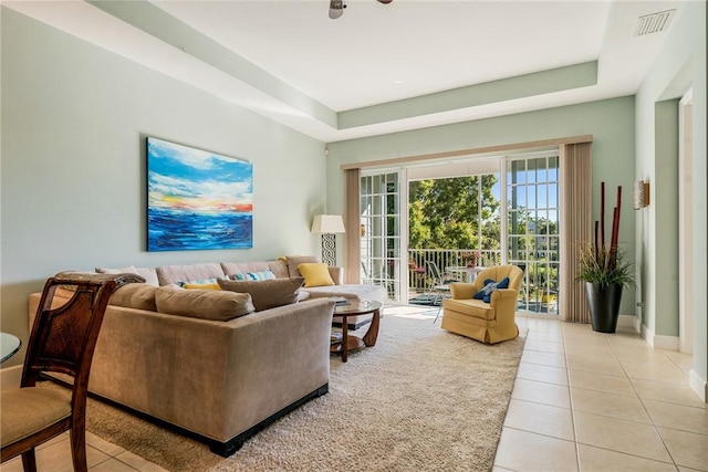 living room featuring light tile patterned floors, visible vents, a raised ceiling, and baseboards