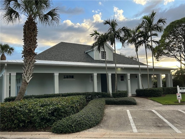 view of front of house with uncovered parking, roof with shingles, and stucco siding