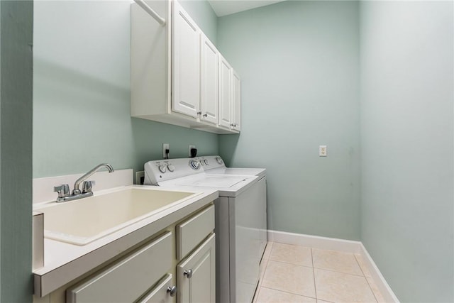 clothes washing area with light tile patterned floors, baseboards, washing machine and clothes dryer, cabinet space, and a sink