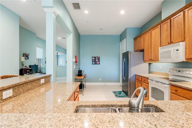 kitchen featuring a sink, white appliances, brown cabinetry, light stone countertops, and ornate columns