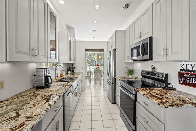 kitchen featuring light tile patterned flooring, sink, appliances with stainless steel finishes, light stone countertops, and white cabinets