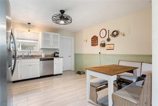 kitchen featuring sink, decorative light fixtures, light wood-type flooring, stainless steel appliances, and white cabinets