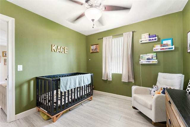 bedroom with a crib, ceiling fan, and light wood-type flooring