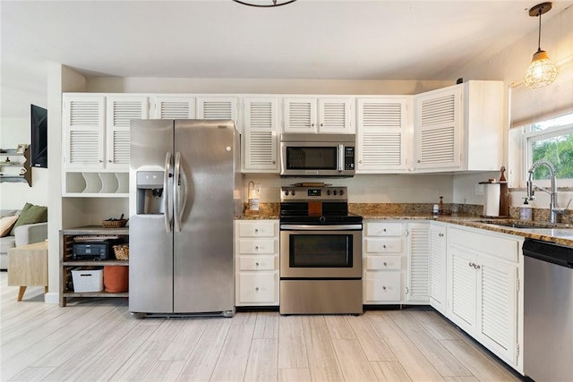 kitchen featuring appliances with stainless steel finishes, decorative light fixtures, white cabinetry, sink, and dark stone countertops