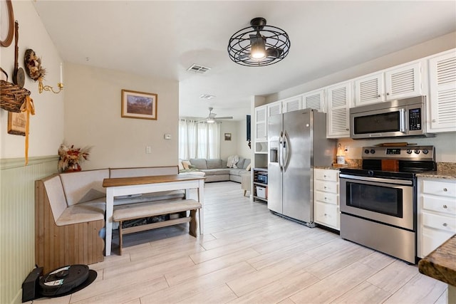 kitchen featuring stone counters, appliances with stainless steel finishes, white cabinetry, ceiling fan, and light hardwood / wood-style floors