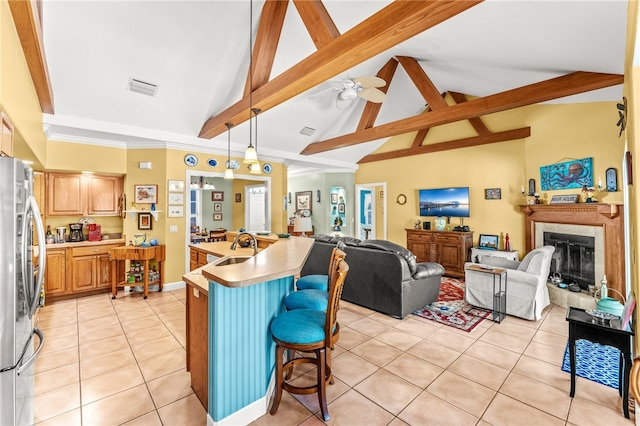 kitchen featuring light tile patterned flooring, a breakfast bar, hanging light fixtures, stainless steel refrigerator, and a kitchen island with sink