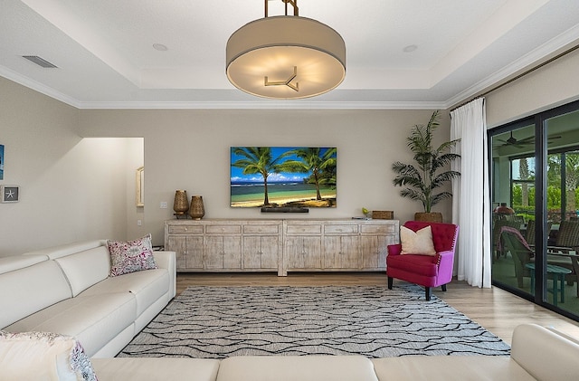 living room featuring ornamental molding, a tray ceiling, and light hardwood / wood-style floors