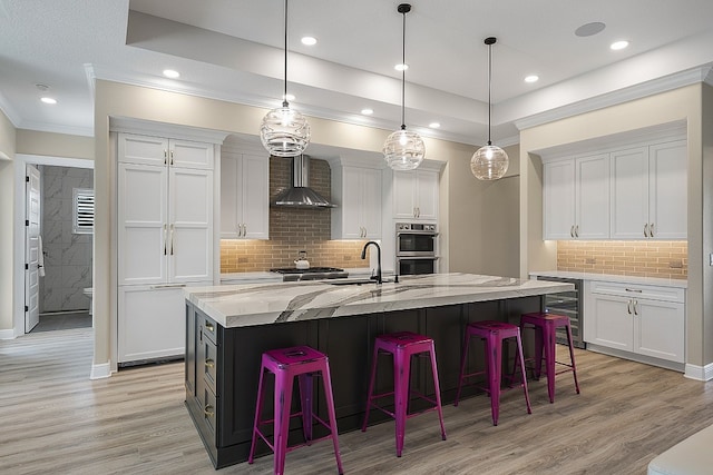 kitchen featuring white cabinets, wall chimney exhaust hood, light hardwood / wood-style floors, and a kitchen island with sink