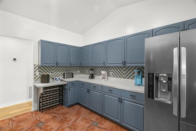 kitchen with stainless steel fridge with ice dispenser, backsplash, blue cabinetry, and lofted ceiling